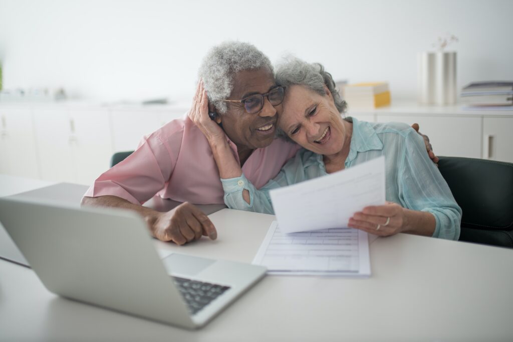 Smiling elderly couple embracing while looking at laptop and documents celebrating approved medical benefits in Pomona California workers compensation case